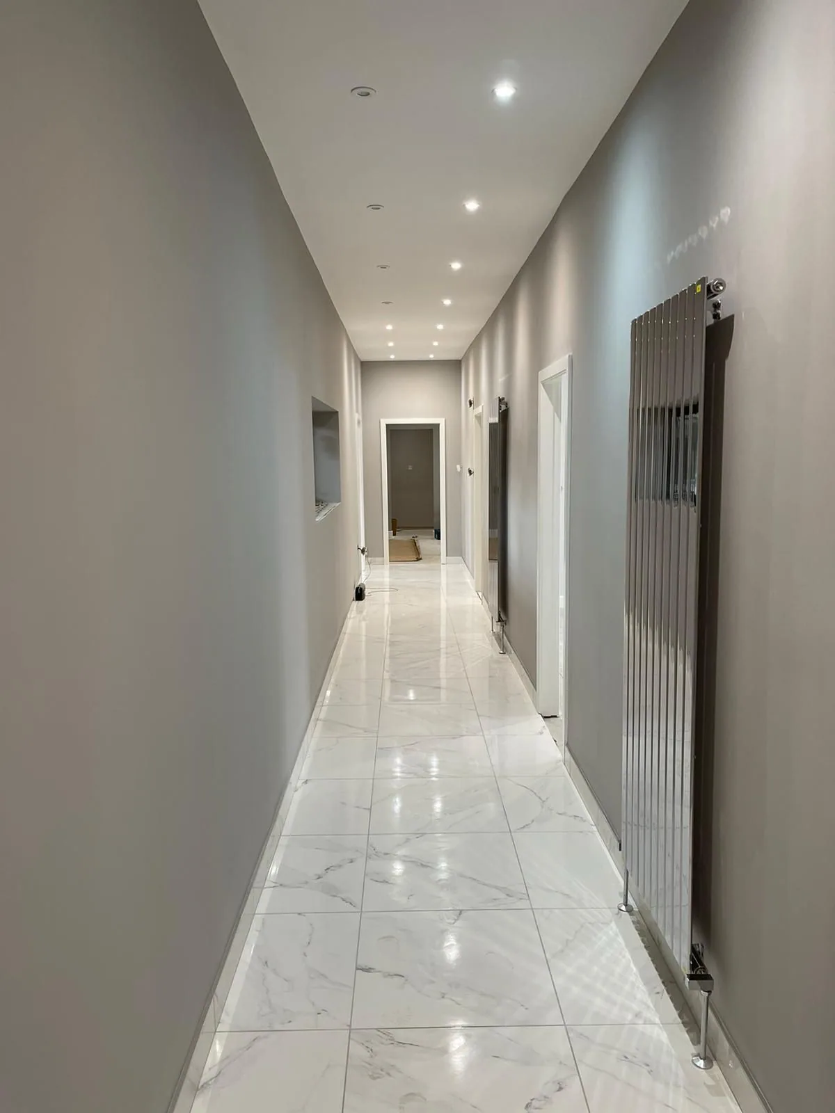 Same corridor finished with crisp white ceiling, warm grey walls and polished marble flooring